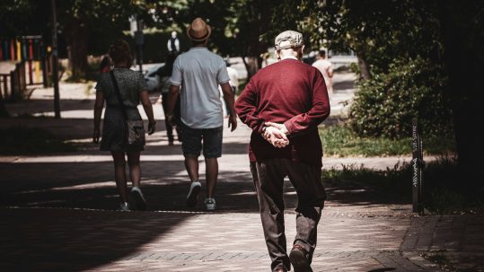 elderly man walking away with hands behind back