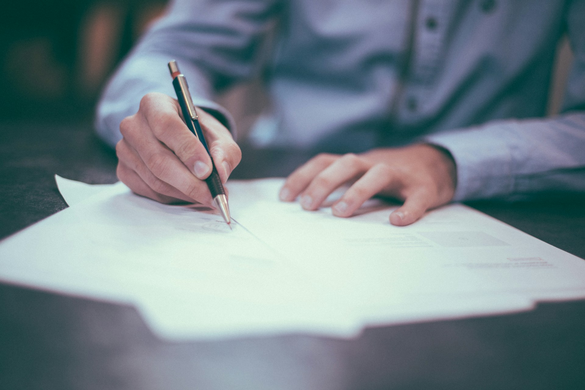 a man's hands signing a document on a desk